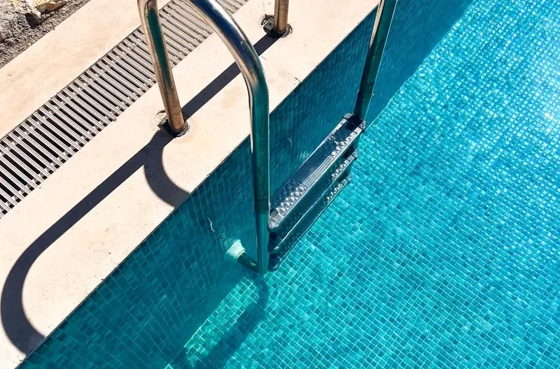 Pormenor de piscina tratada: degrau em mosaico azul, linha de água limpa e caleira de transbordo sem resíduos